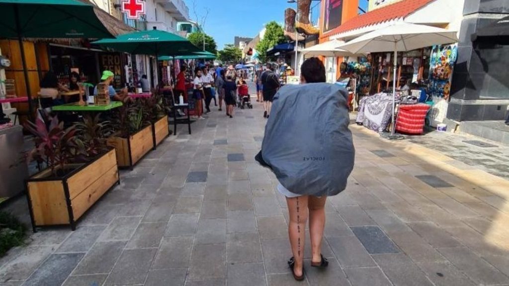 L'autrice du blog porte sur son dos un énorme sac à dos. Elle est dans une rue passante et commerçante.