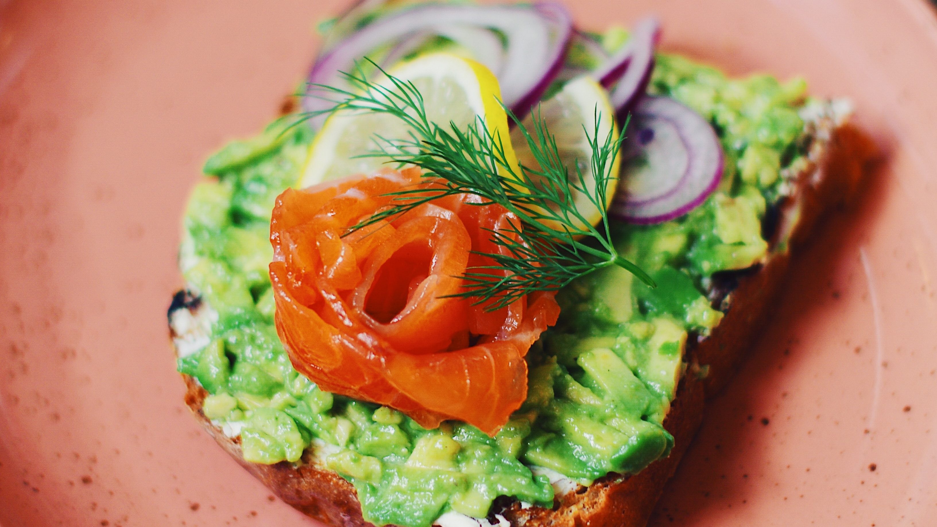 Une tartine de pain, avec une purée d'avocats, des oignons rouges, une rondelle de citron et du saumon