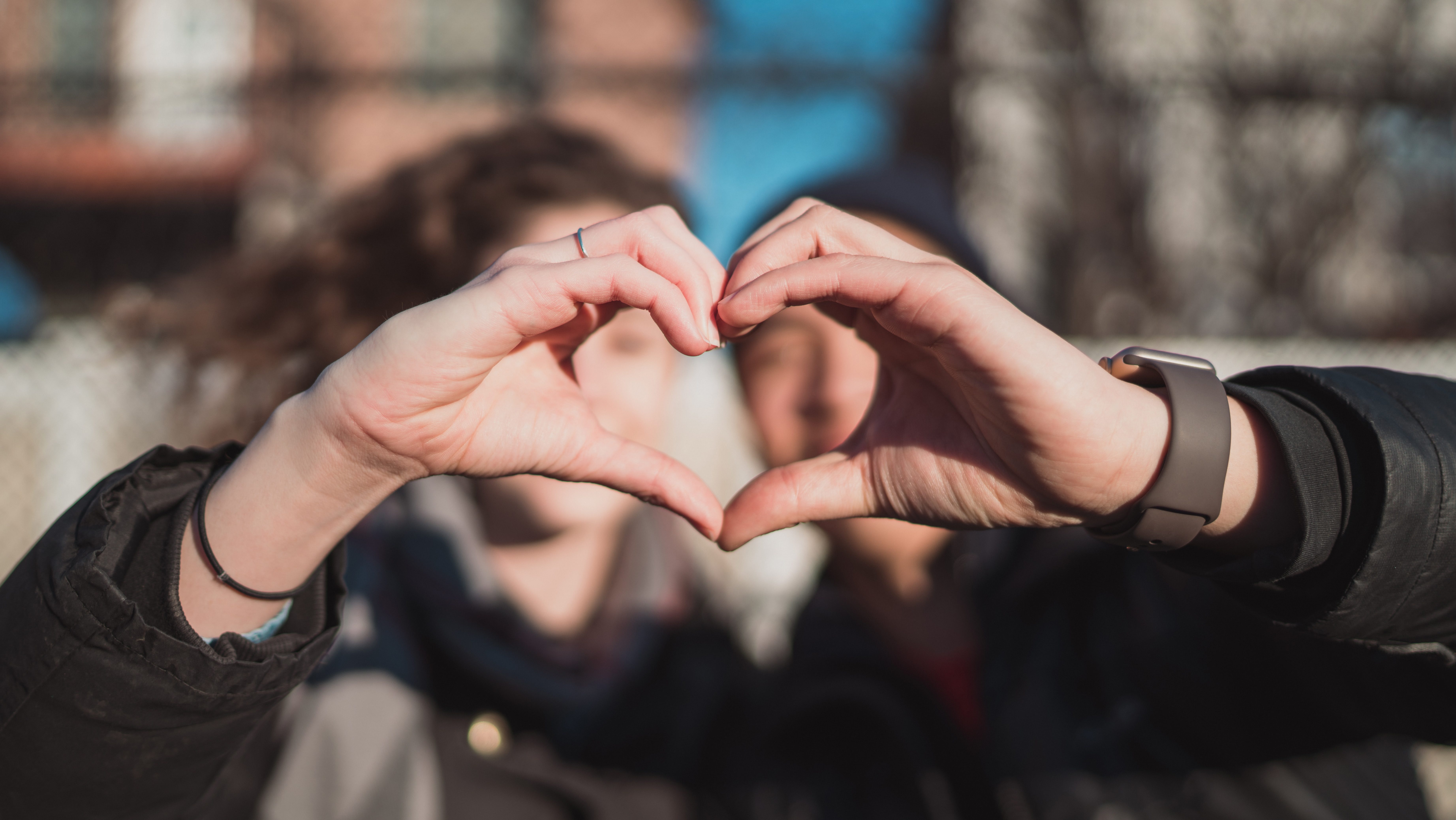 Deux personnes sont en fond floutés. Leurs deux mains ensemble forment un coeur géométrique.